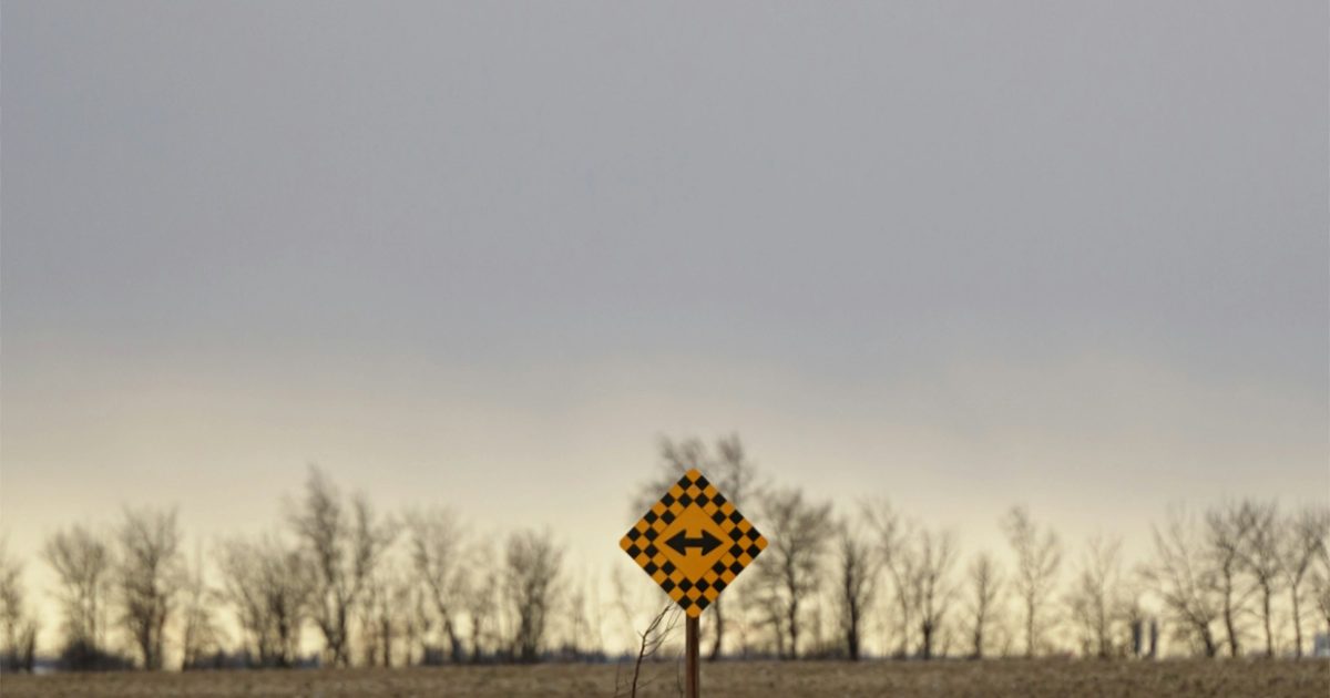 A yellow crossroads sign standing in open countryside
